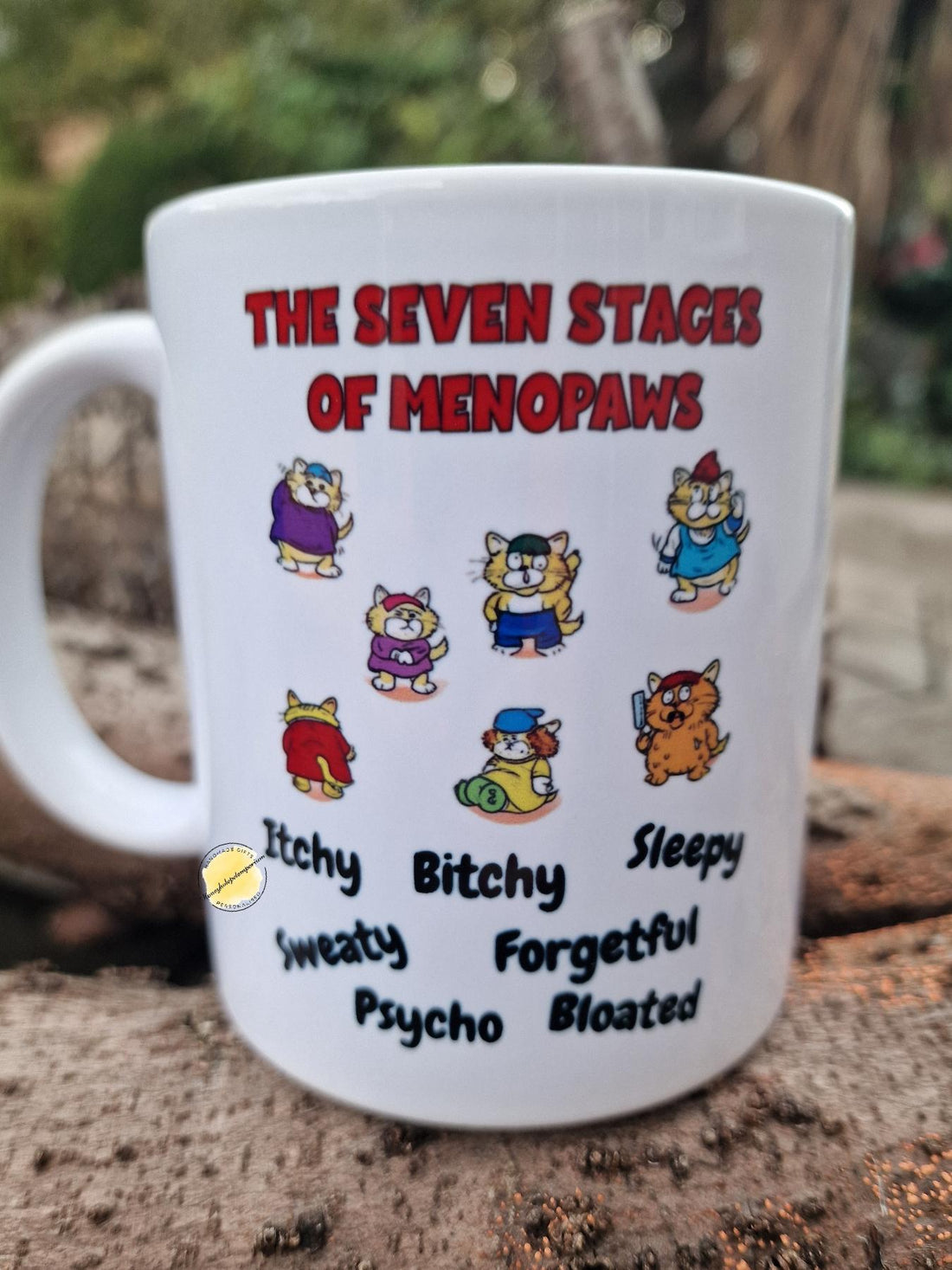 Mug with 'The Seven Stages of Menopaws' design featuring cartoon cats and humorous text.