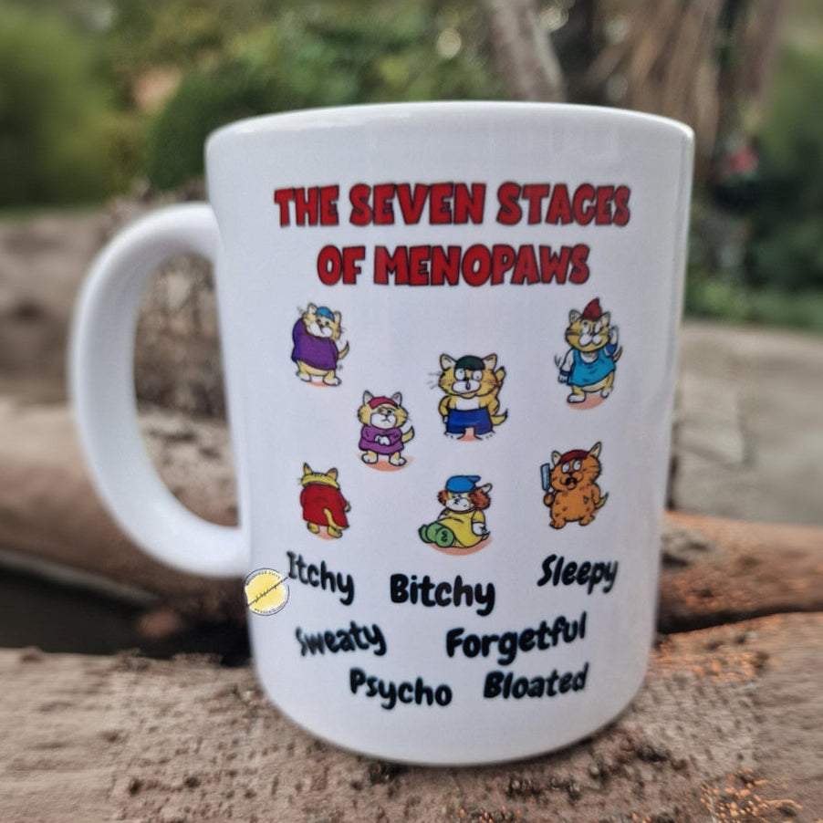 Mug with 'The Seven Stages of Menopaws' design featuring cartoon cats and humorous text.