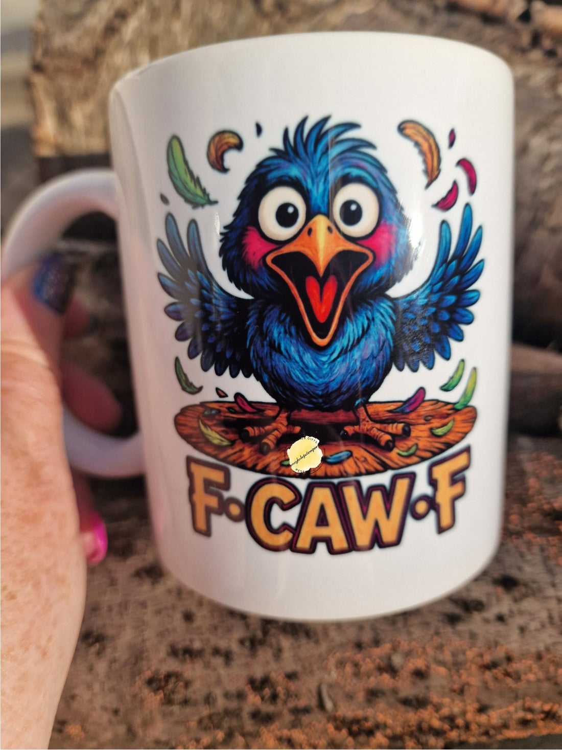 Mug with a colorful bird design and 'F-CAW-F' text held by a person.